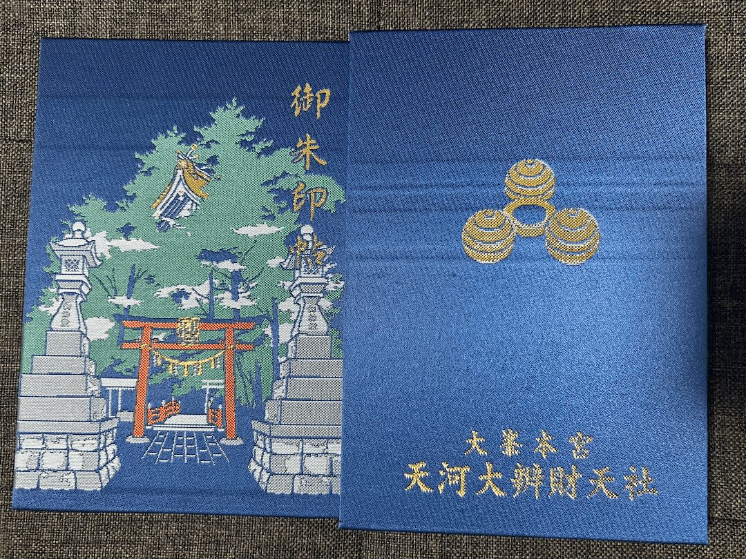 天河大弁財天社の御朱印帳。深い青地に社殿の刺繍と三つ巴の意匠が施された一冊